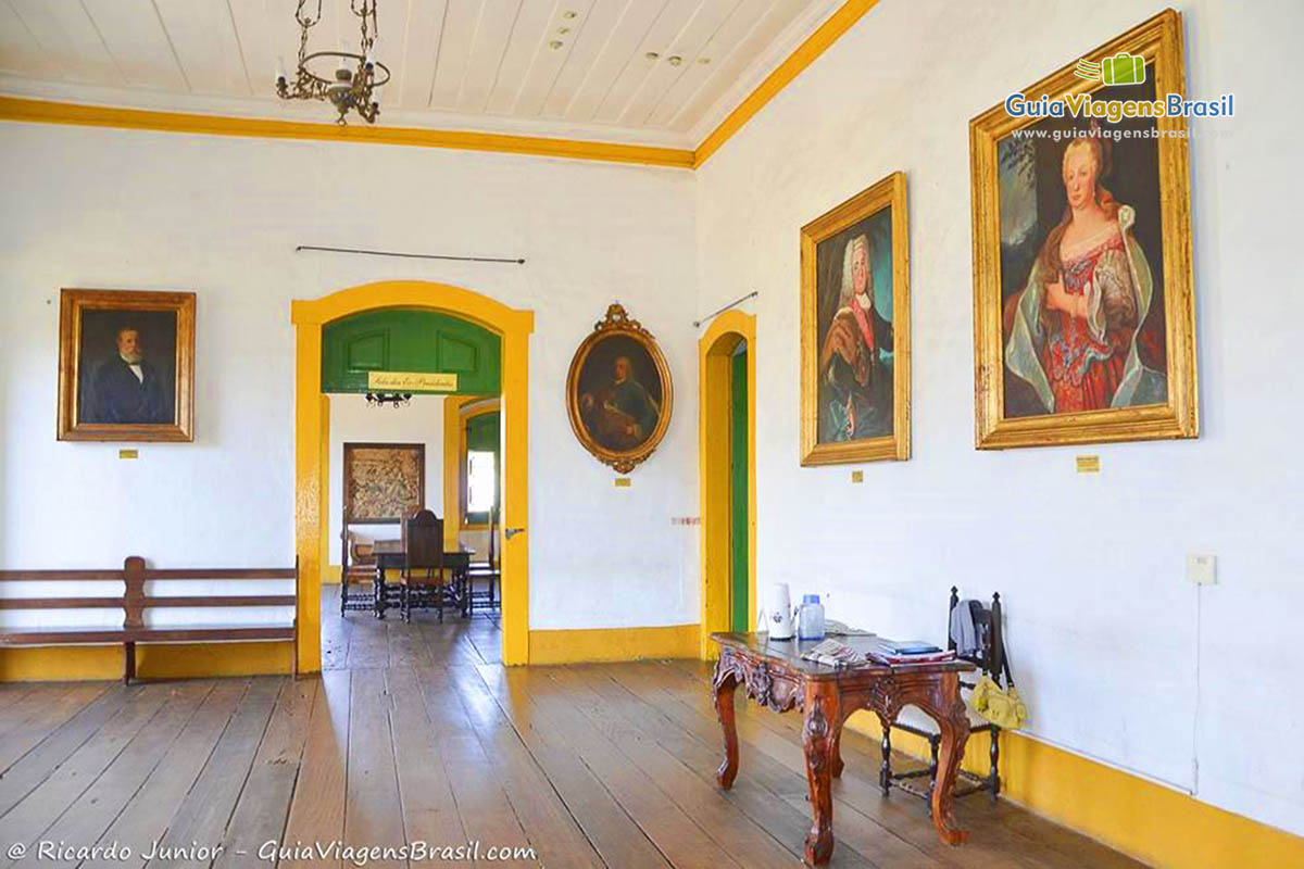 Imagem da sala de entrada, chão de madeira e quadros na parede, contando a história.